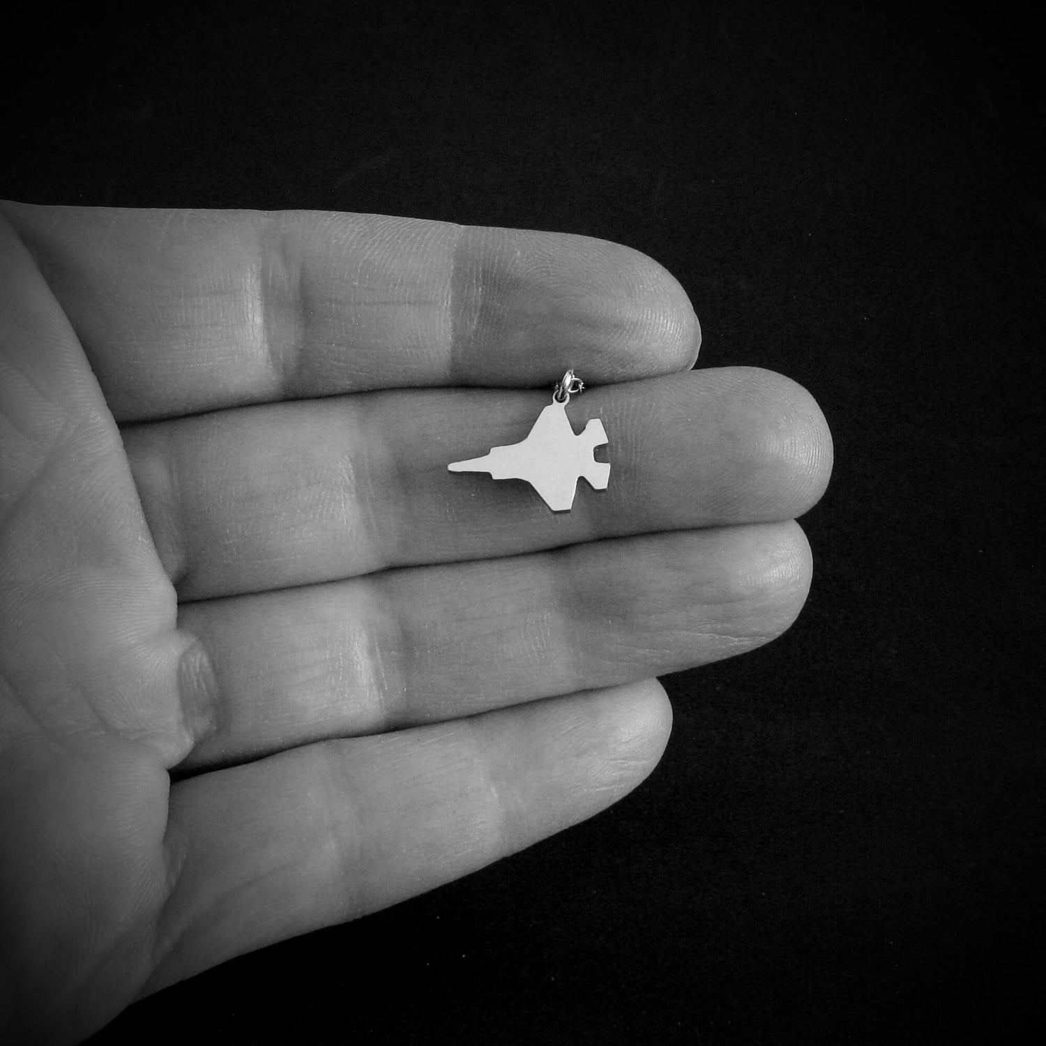 Small F-35 Lightning Military Fighter jet  pendant held in a hand against a black background