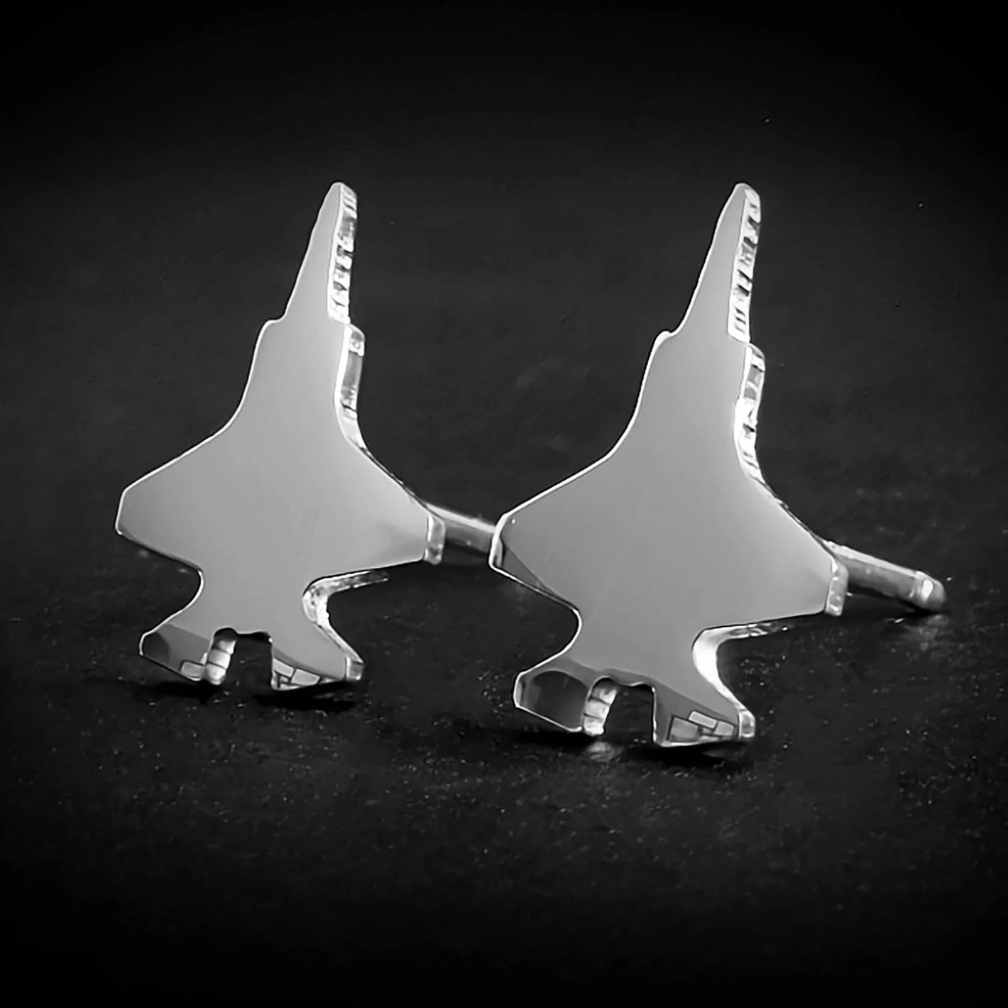 Close-up of shiny F-35 jet silhouette earrings in polished sterling silver on a dark background