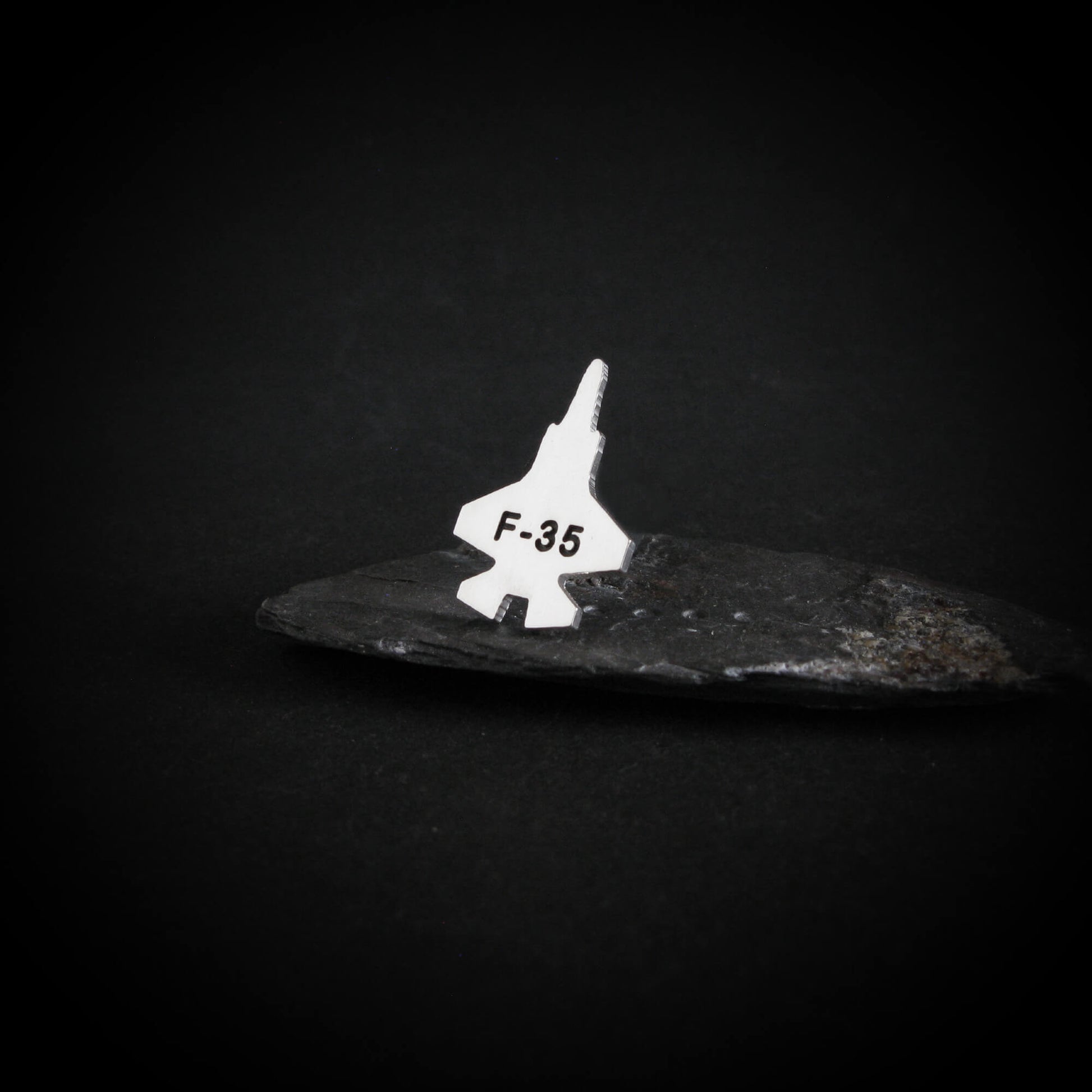Silver F-35 silver tie pin jet airplane on a dark stone surface with a black background