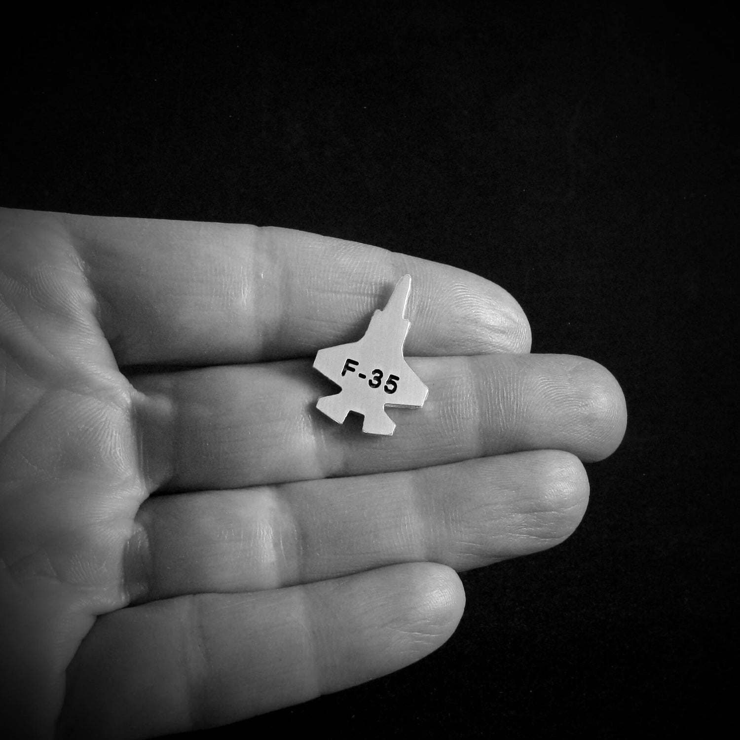 Small F-35 lapel pin jet airplane on a hand against a black background