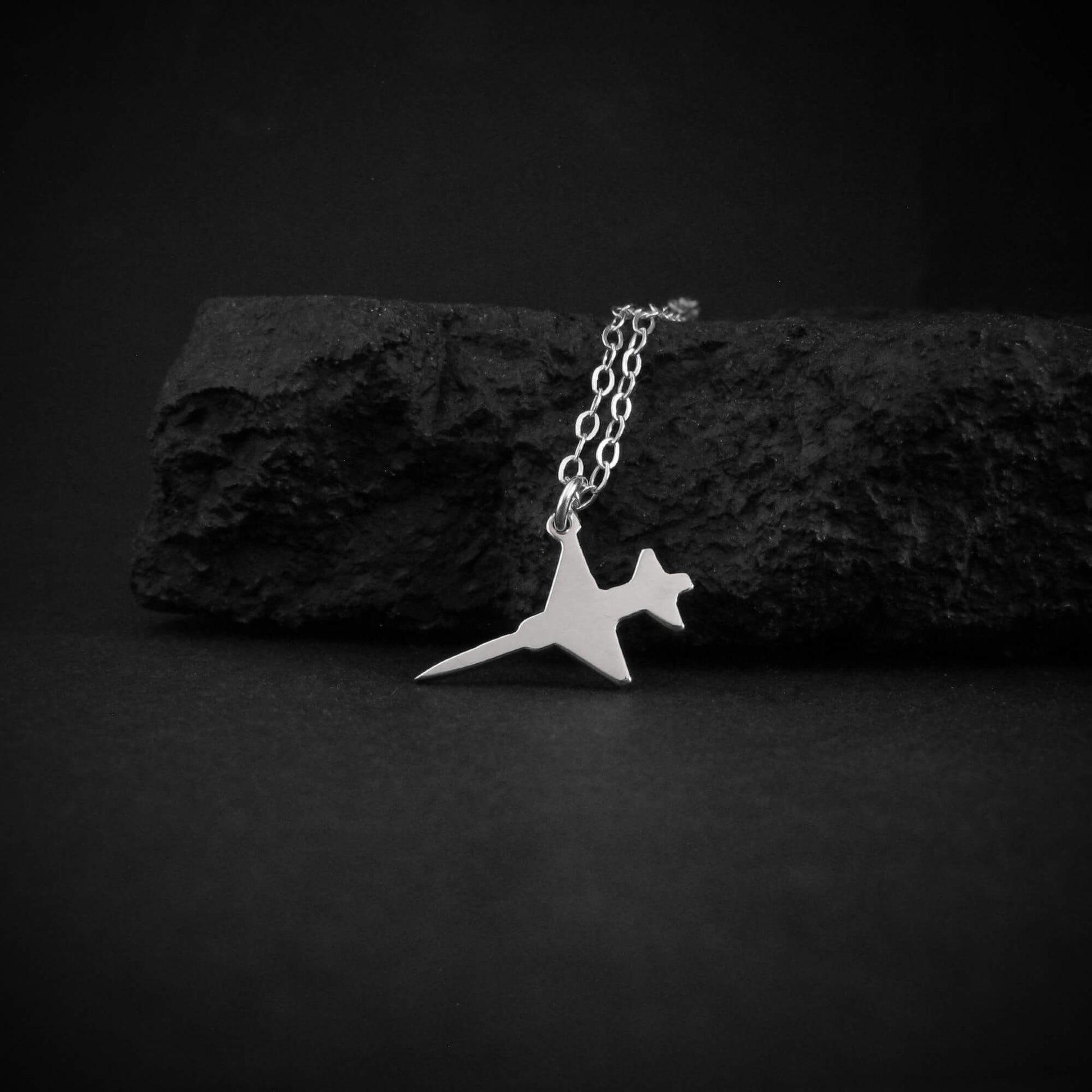 Sterling silver F-5 Freedom Fighter Jet Airplane pendant necklace resting on black rock – handmade military aviation jewelry
