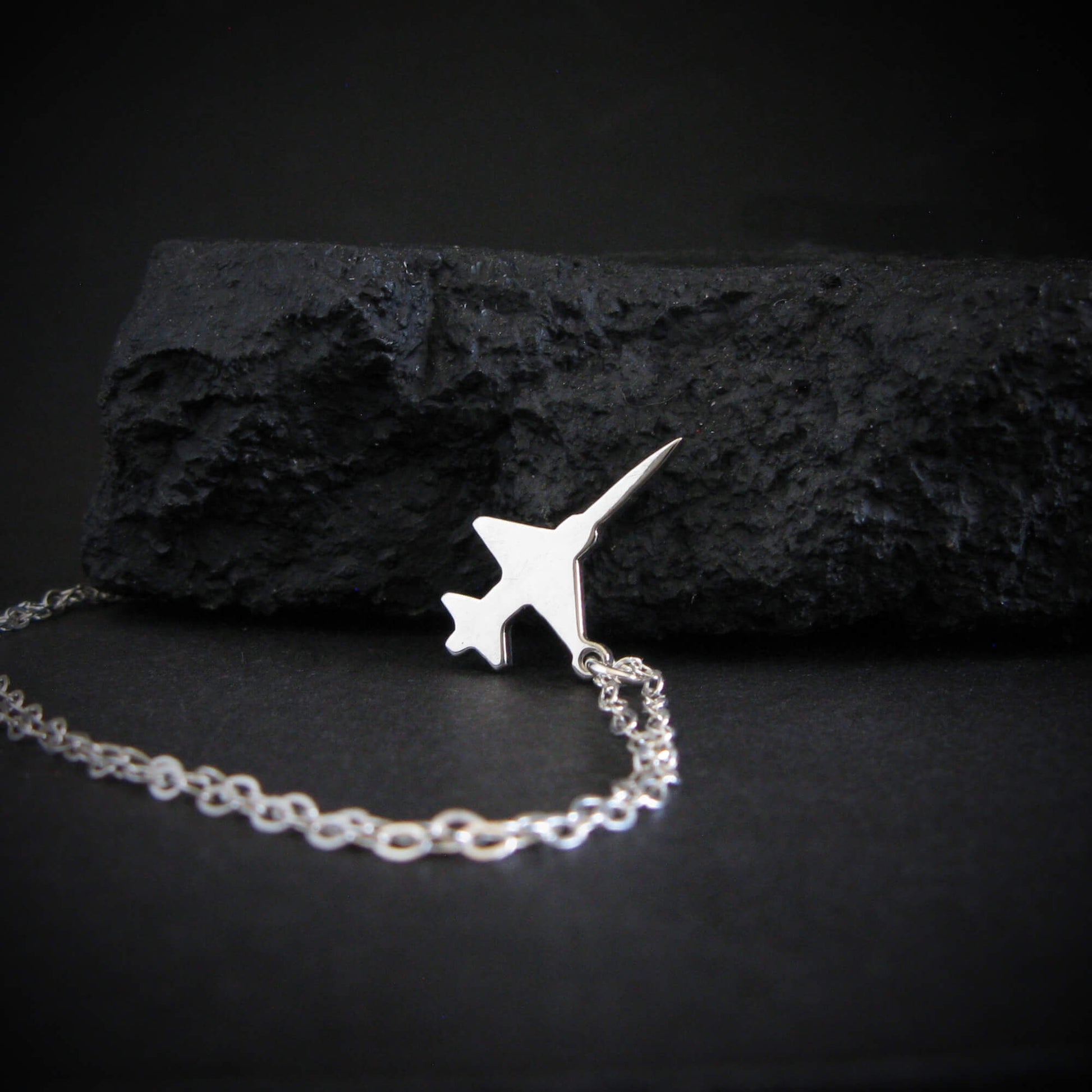 Sterling silver F-5 Freedom Fighter airplane pendant necklace displayed on black rock – artisan aviation jewelry handmade in USA