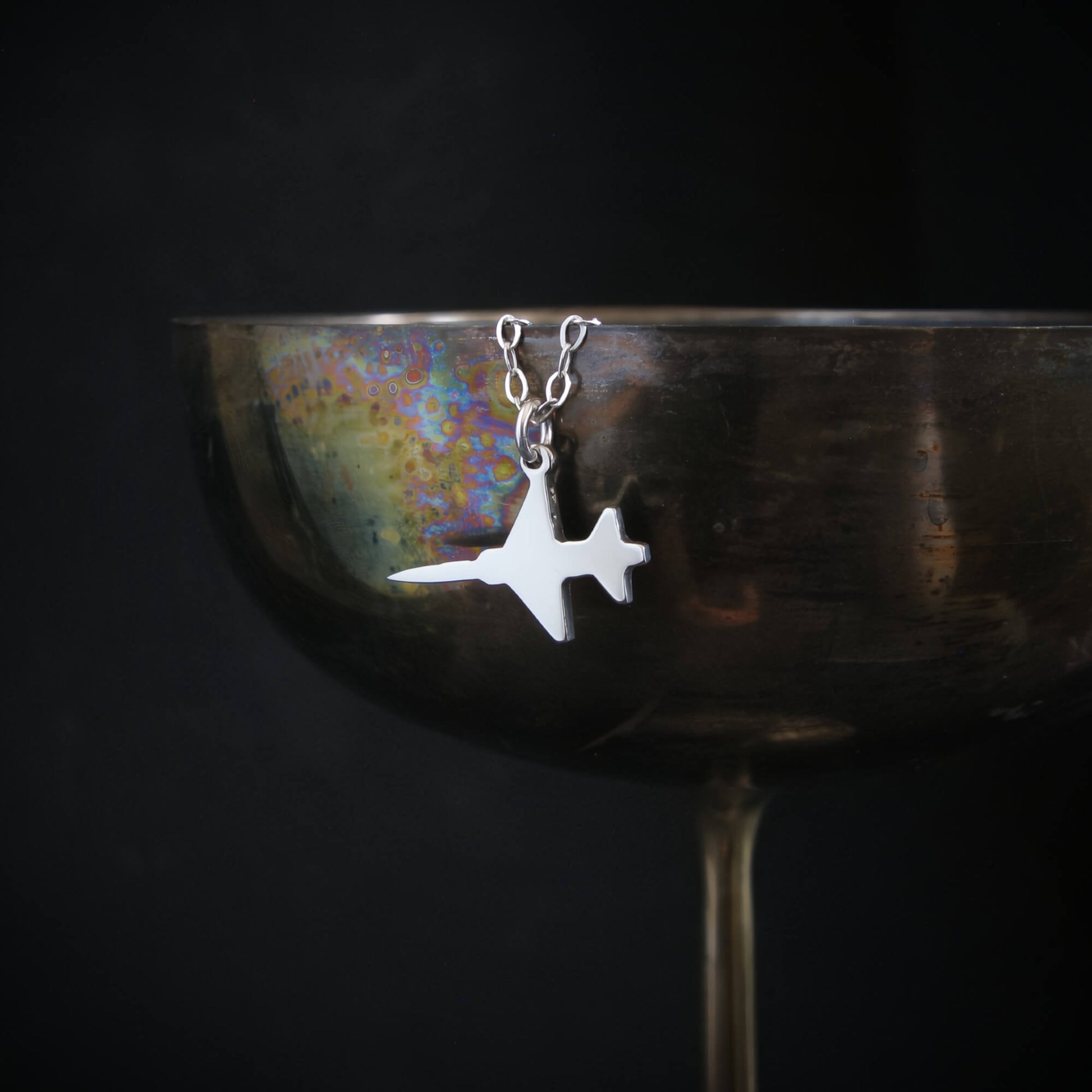 Sterling silver F-5 Freedom Fighter jet pendant necklace displayed on wine glass – handcrafted aviation jewelry photography