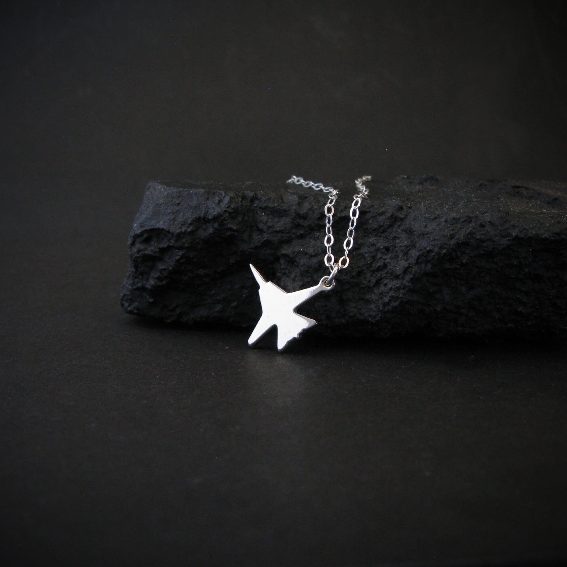 Sterling silver F-14 Tomcat jet fighter pendant necklace displayed on black rock, handcrafted aviation jewelry