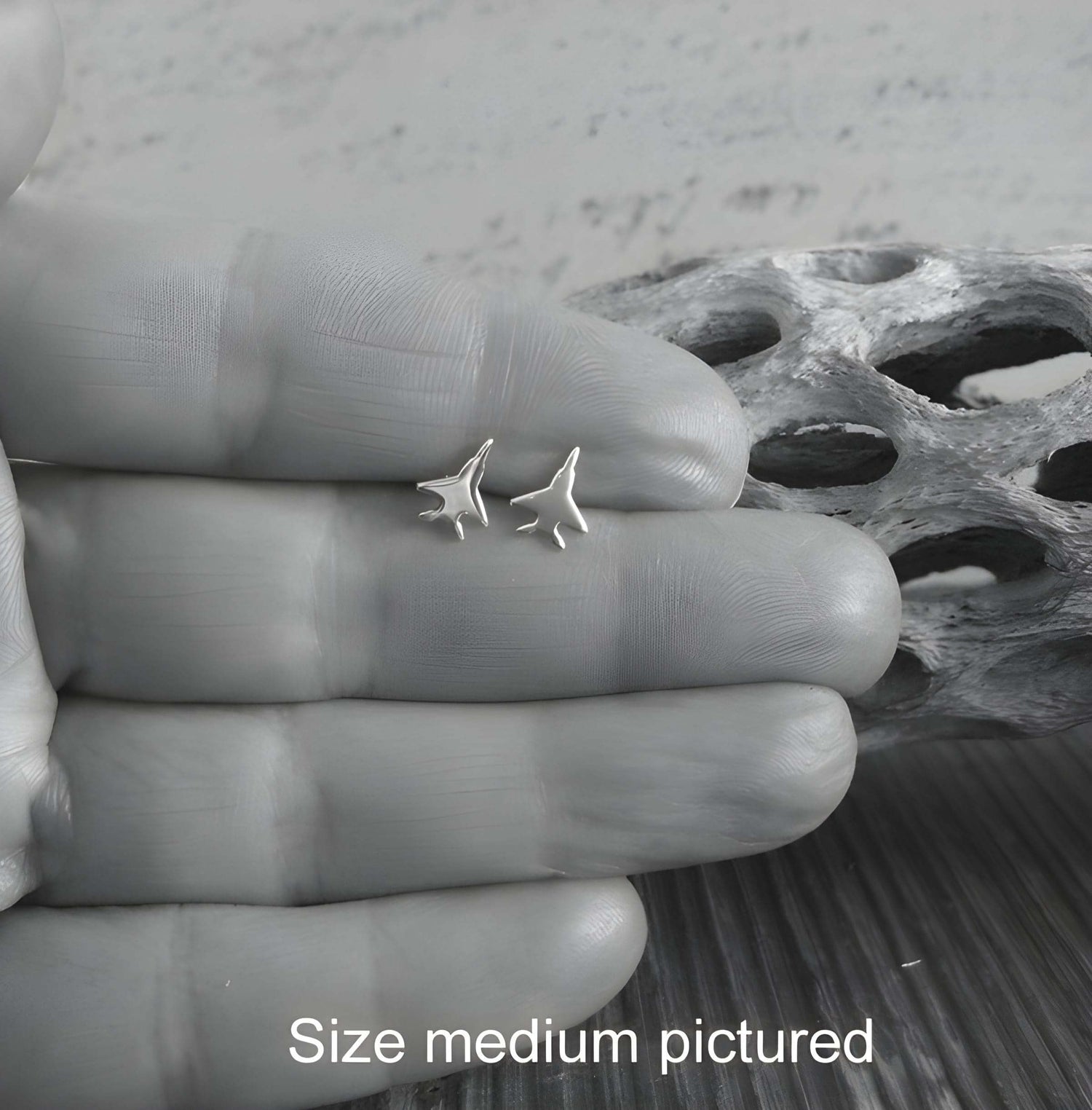 Pair of sterling silver F-15 Eagle stud earrings held in a hand  for size reference 