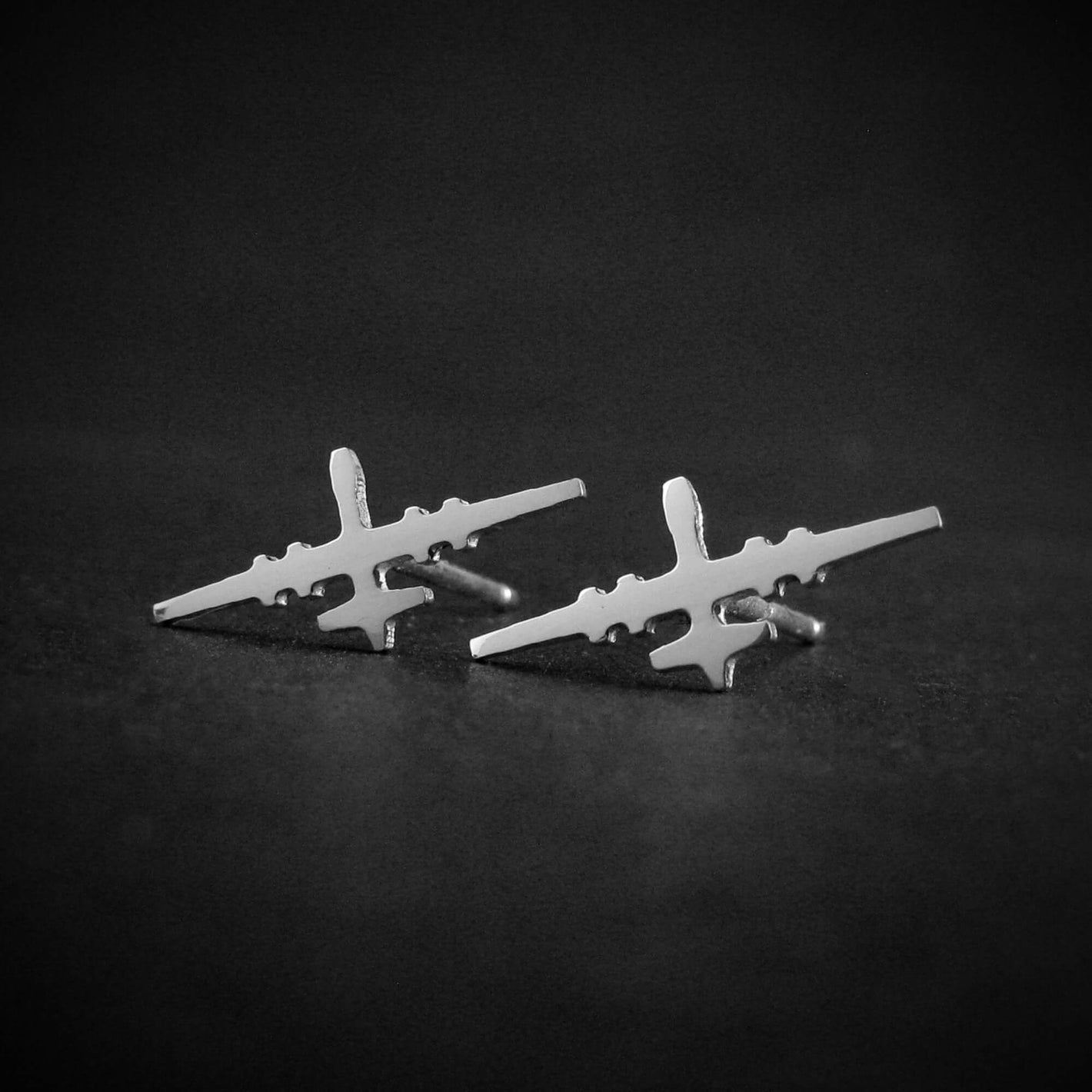 Sterling silver stud earrings shaped like the MQ-9 Reaper military drone, handmade with detailed aircraft silhouette, displayed on a dark background.
