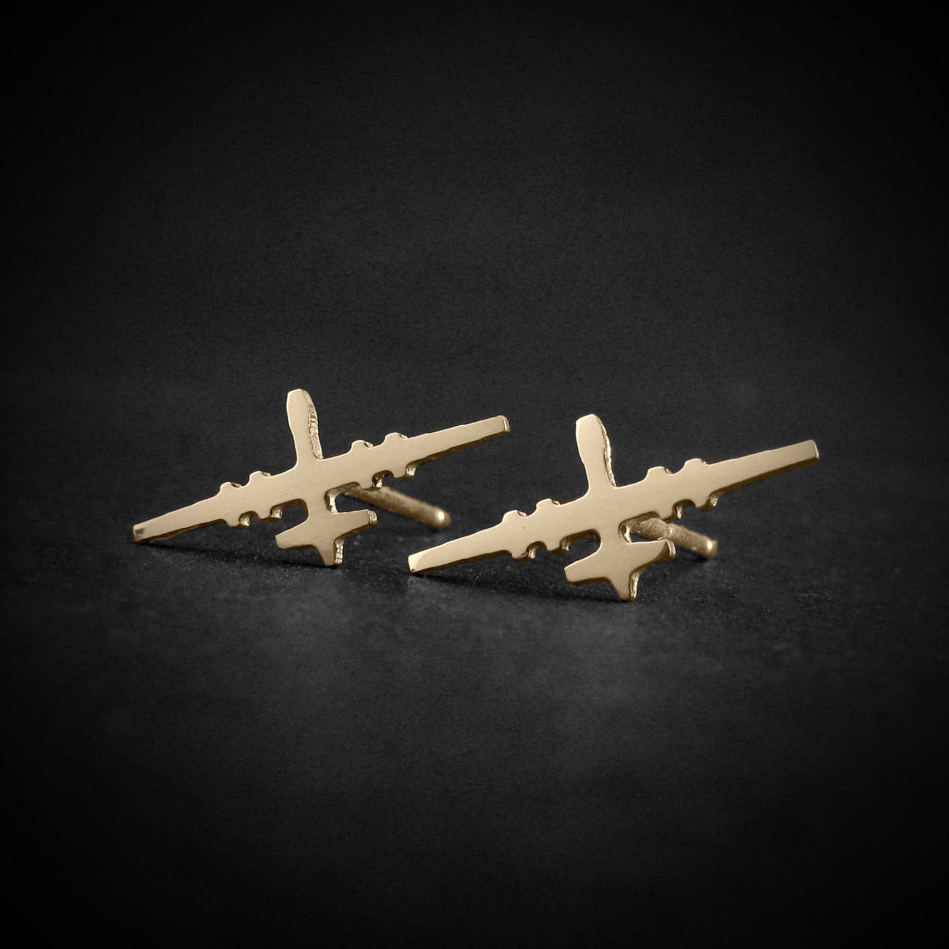 14k gold stud earrings in the shape of the MQ-9 Reaper military drone, handcrafted with precision aircraft detailing, set against a dark background.