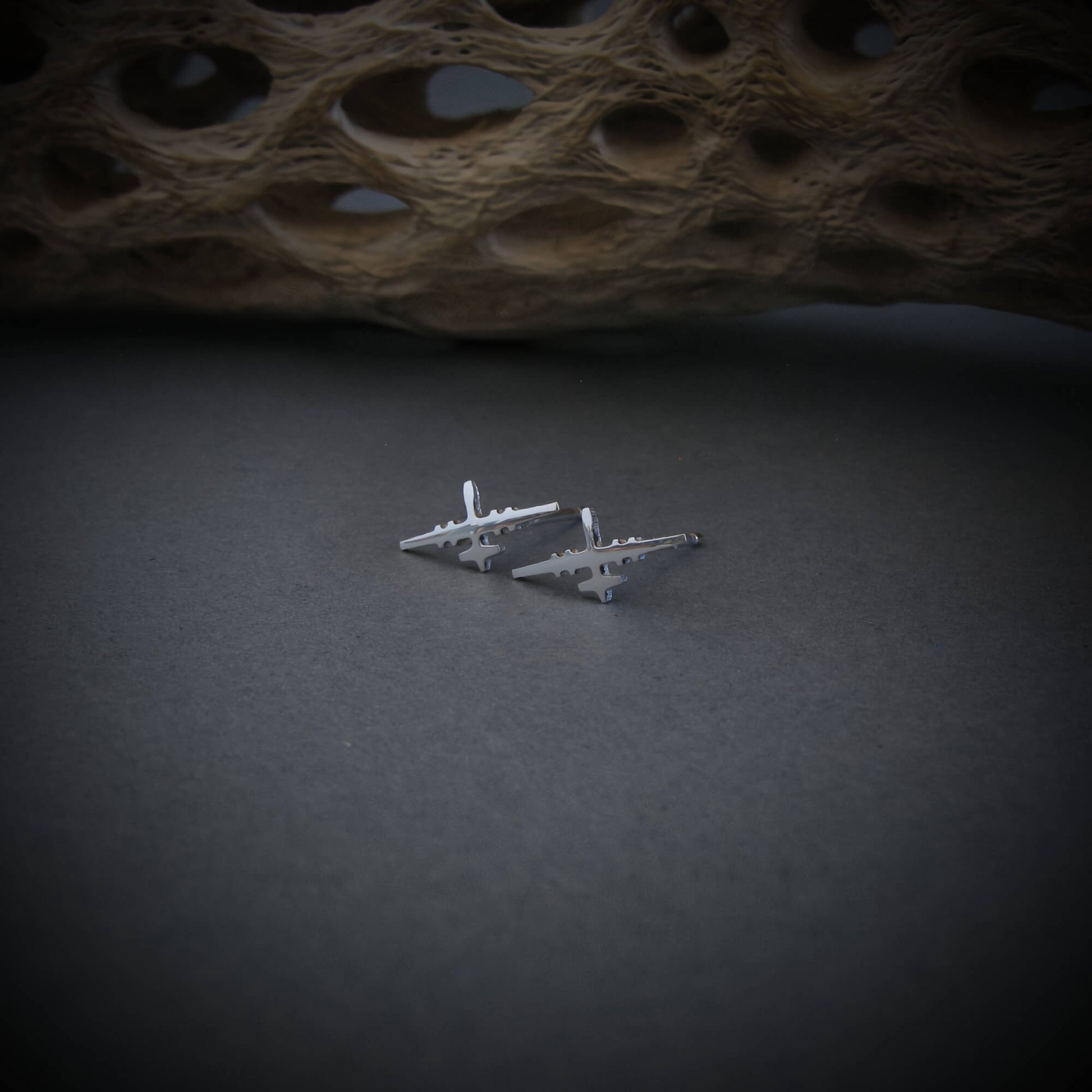 Polished sterling silver MQ-9 Reaper drone stud earrings, handcrafted with aircraft detailing, displayed on a dark surface with natural textured background.