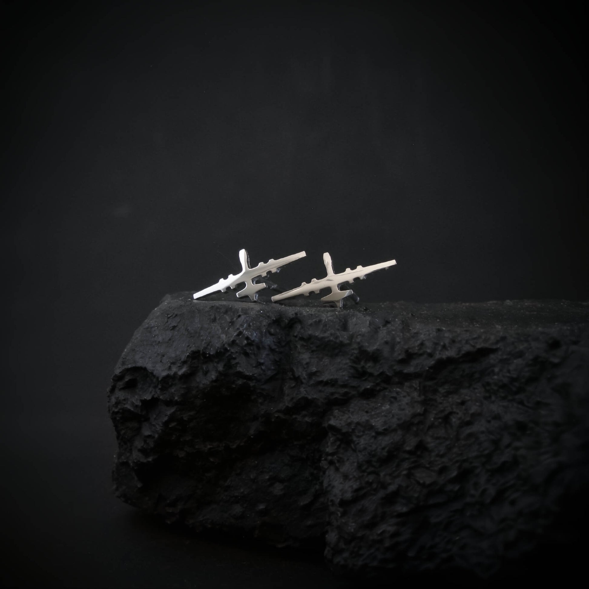 Sterling silver MQ-9 Reaper drone stud earrings, handcrafted with precision, displayed on a rugged black rock against a dark background.