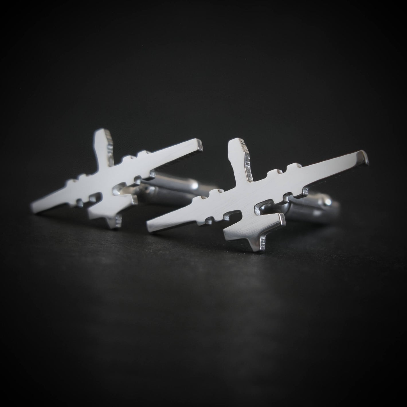 Close-up of polished sterling silver MQ-9 Reaper cufflinks with jet silhouette design on black surface