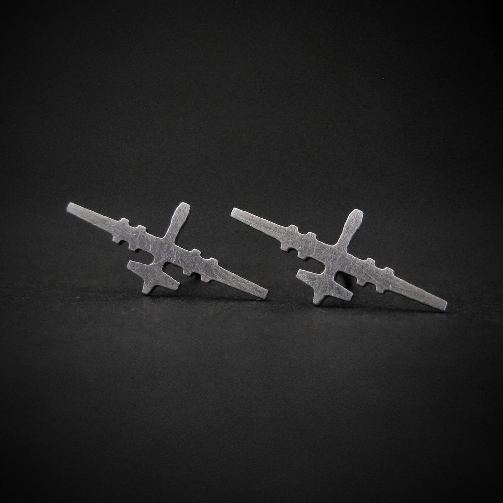 Antiqued sterling silver stud earrings shaped like the MQ-9 Reaper military drone, featuring a matte, vintage-style finish and handcrafted detailing, displayed on a dark background.