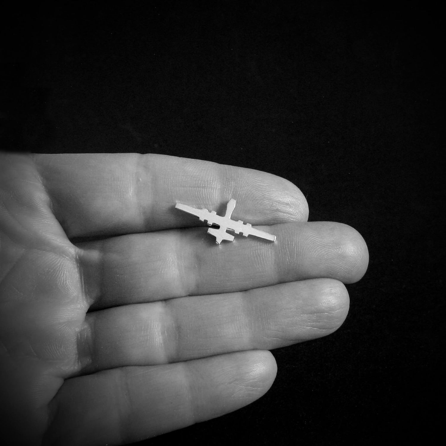 Small MQ-9 Reaper Drone airplane lapel pin held in a hand against a black background