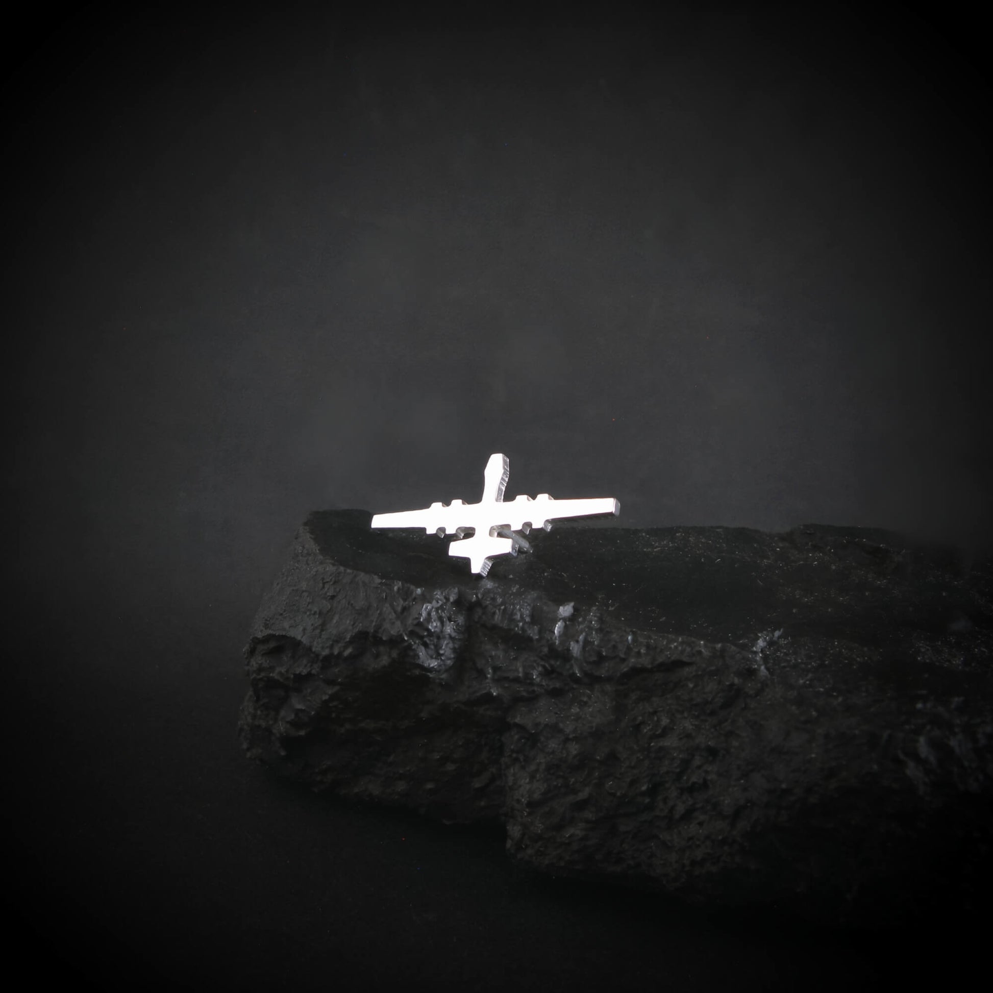Silver MQ-9 Reaper Military Drone airplane tie pin on a dark rock with a dark background