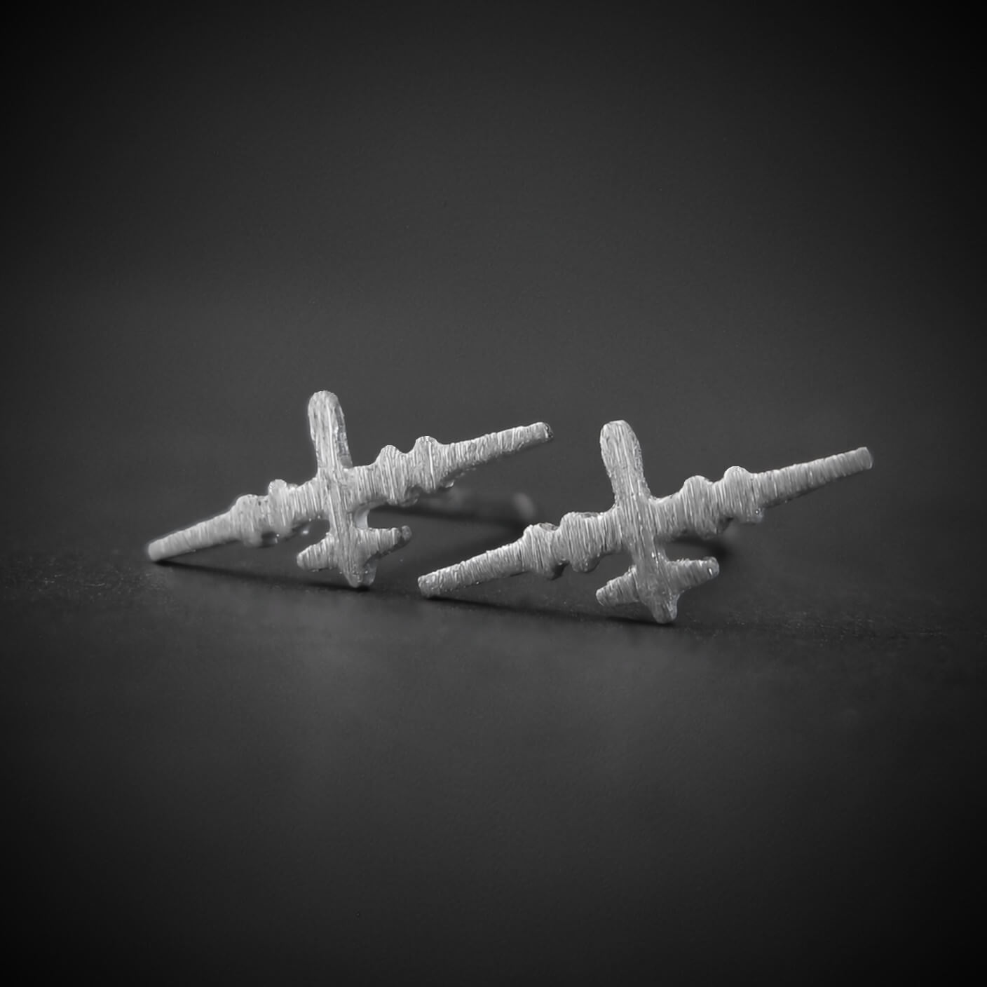 Brushed sterling silver stud earrings shaped like the MQ-9 Reaper military drone, featuring a textured finish and handcrafted detailing, displayed on a dark background.