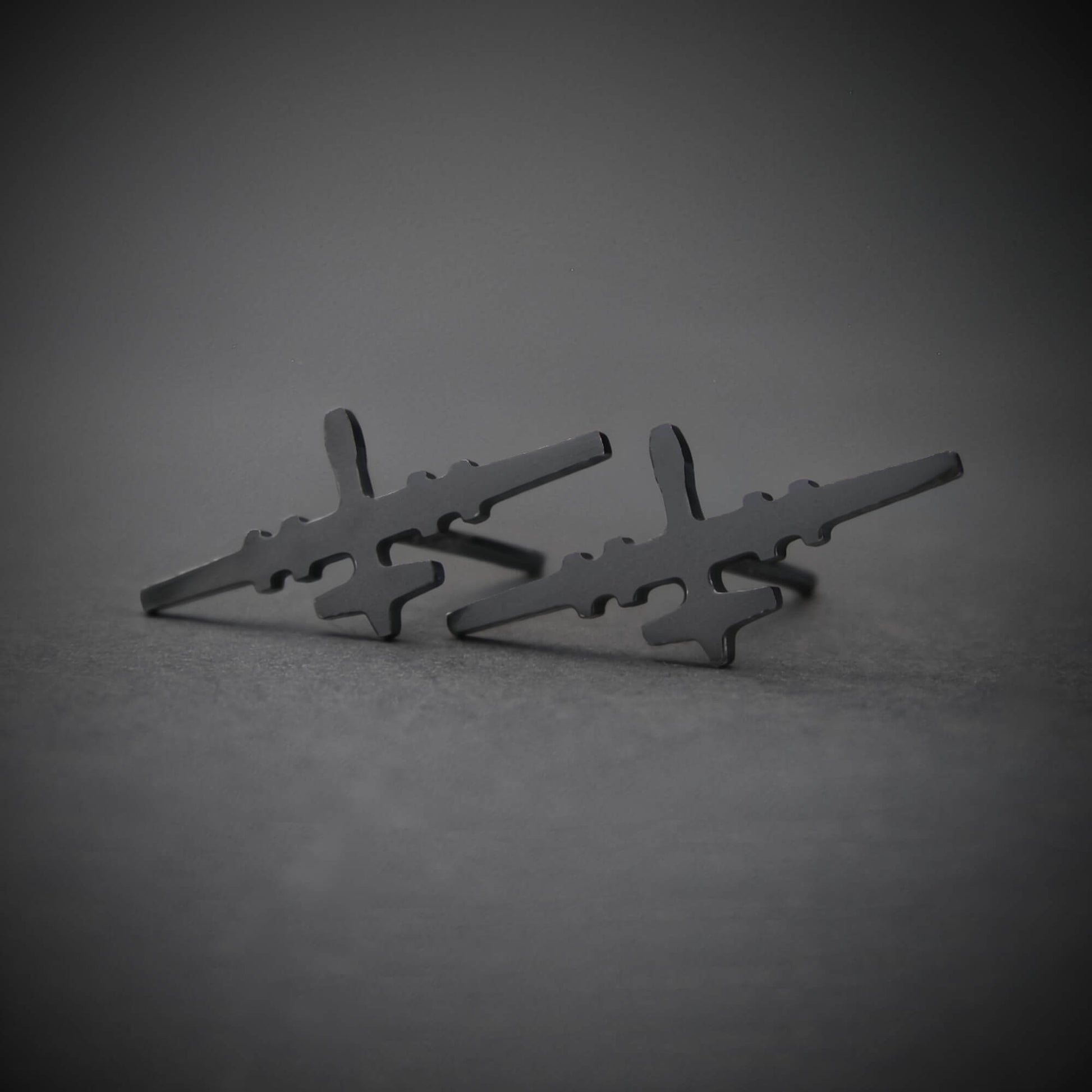 Oxidized sterling silver stud earrings shaped like the MQ-9 Reaper military drone, featuring a sleek dark finish and handcrafted aircraft silhouette, displayed on a gray background.
