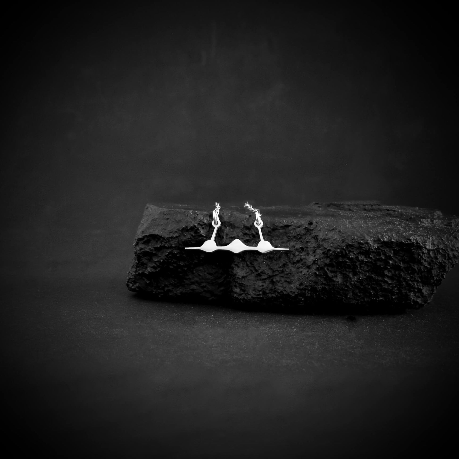 SR-71 front silhouette necklace in sterling silver resting on black volcanic-style stone