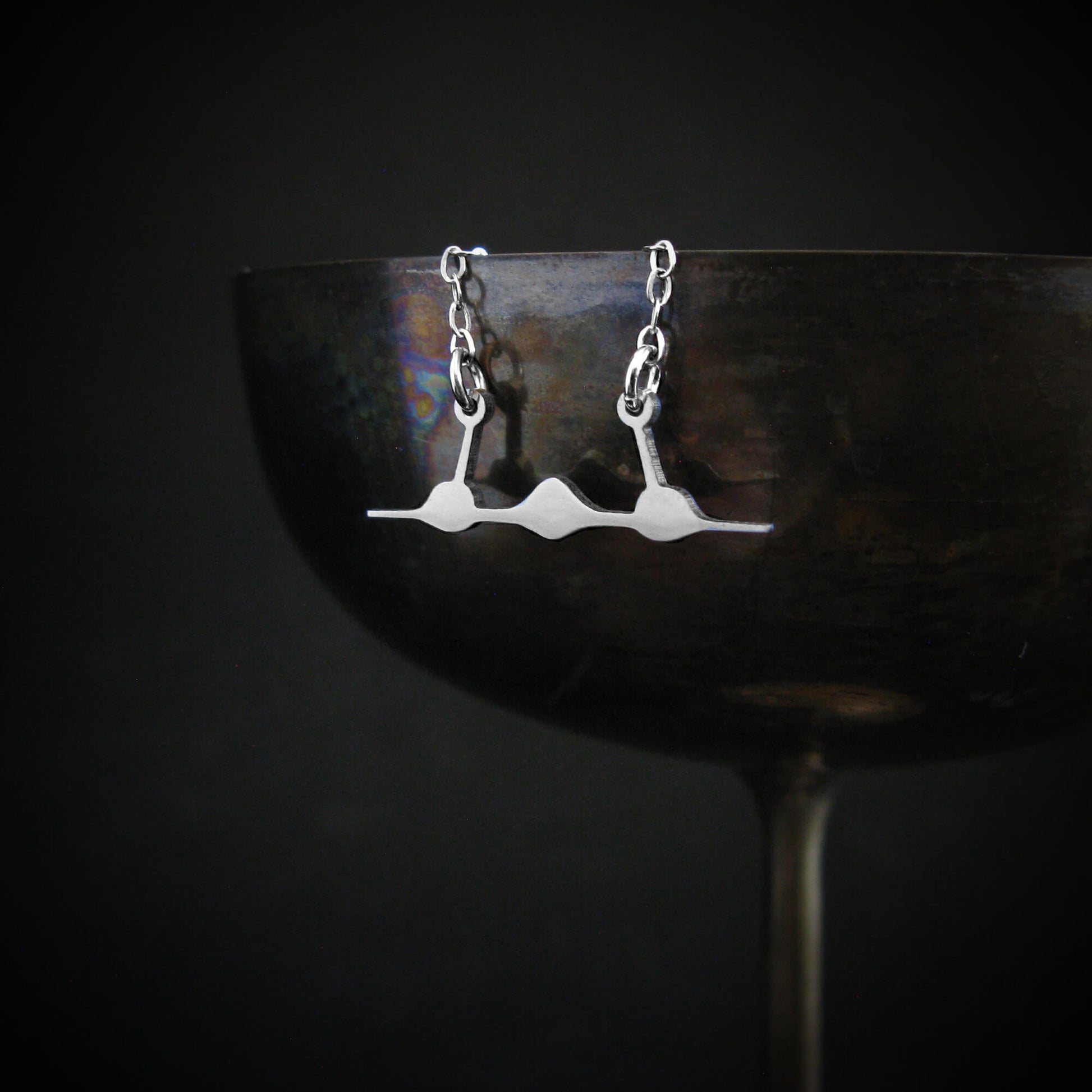 Handmade sterling silver SR-71 Blackbird pendant hanging from rim of vintage metal goblet