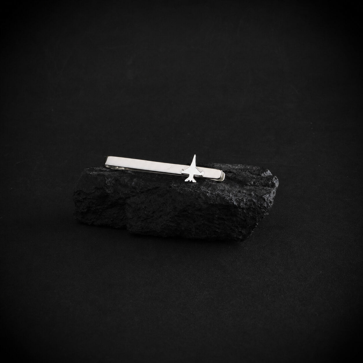 Sterling silver F 16 motif tie bar on a black rock with a black background