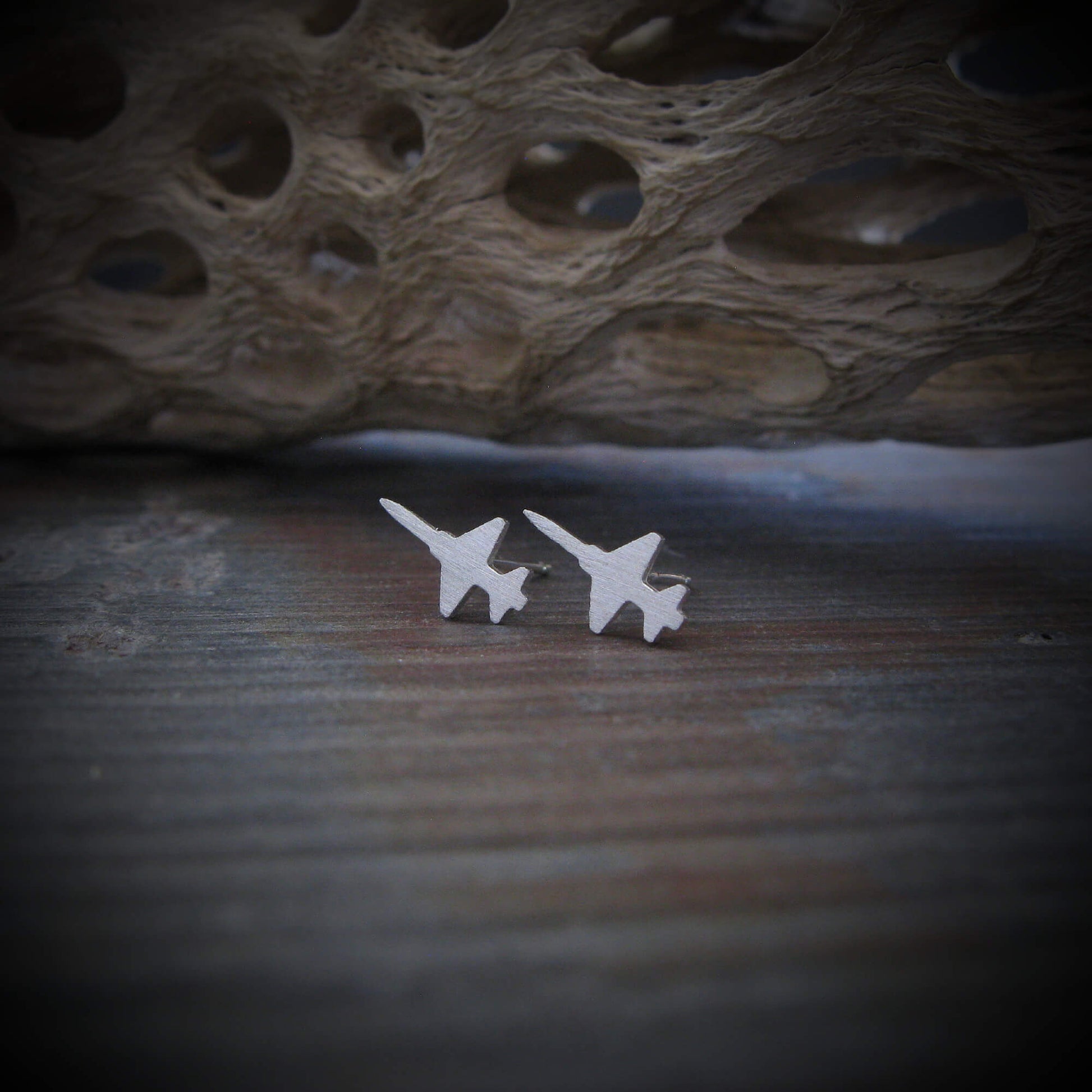 Brushed sterling silver T-38 Talon jet stud earrings displayed on a rustic wooden surface with a textured natural backdrop.
