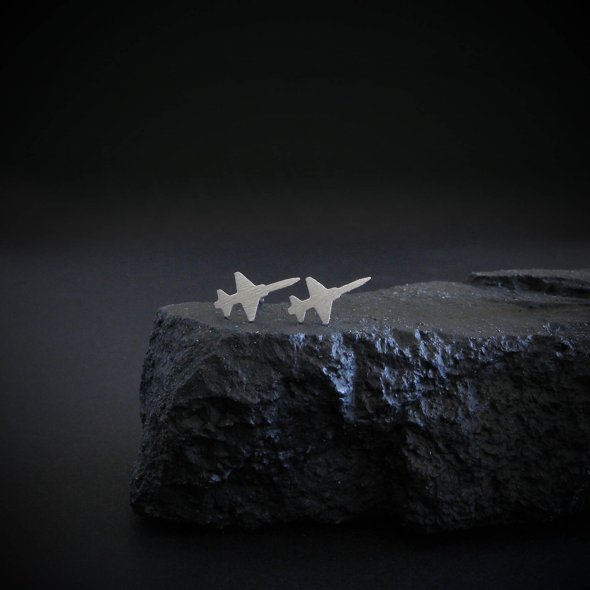 Brushed sterling silver T-38 Talon stud earrings—military jet-inspired aviation handcrafted  jewelry displayed on a rugged black stone with dramatic lighting