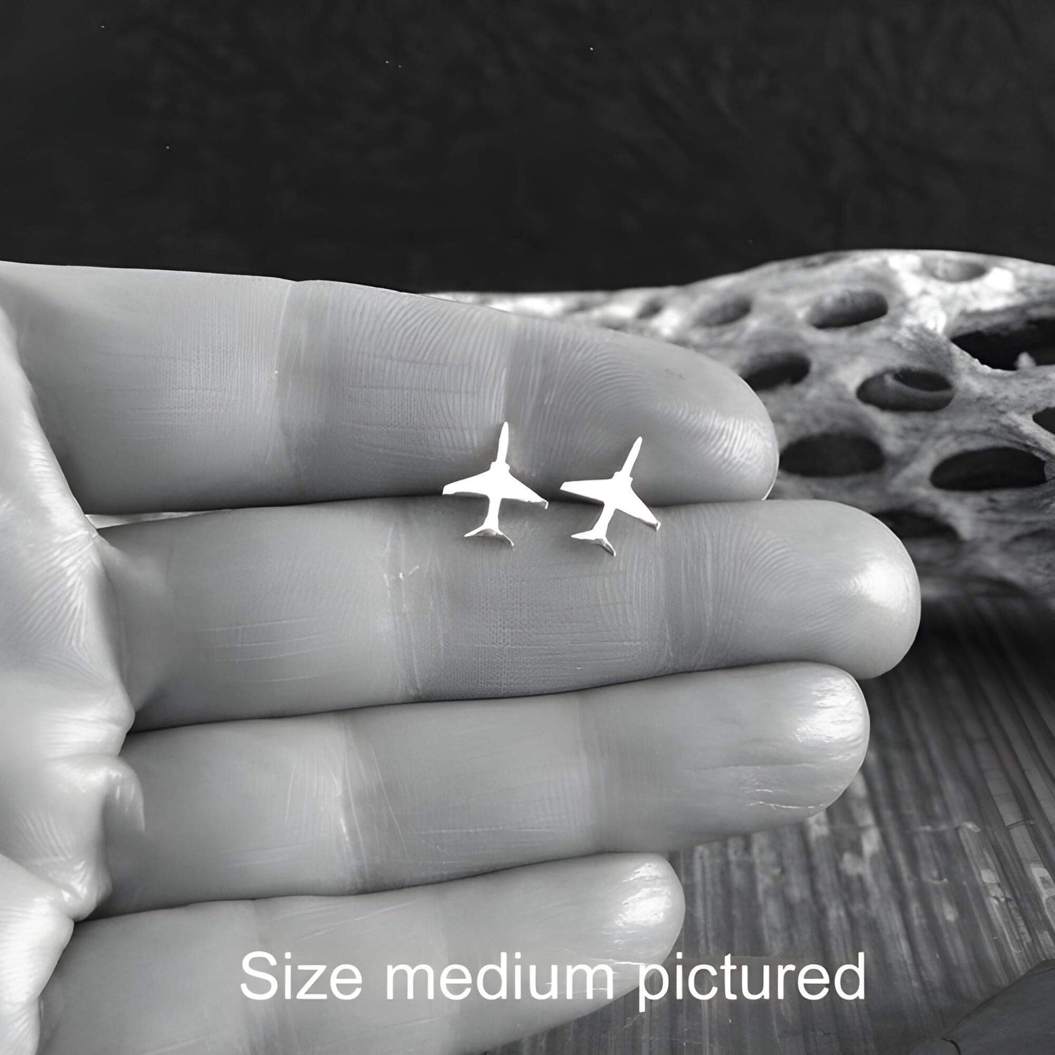 Pair of sterling silver T-45 Jet Fighter stud earrings held in a hand between fingers close up