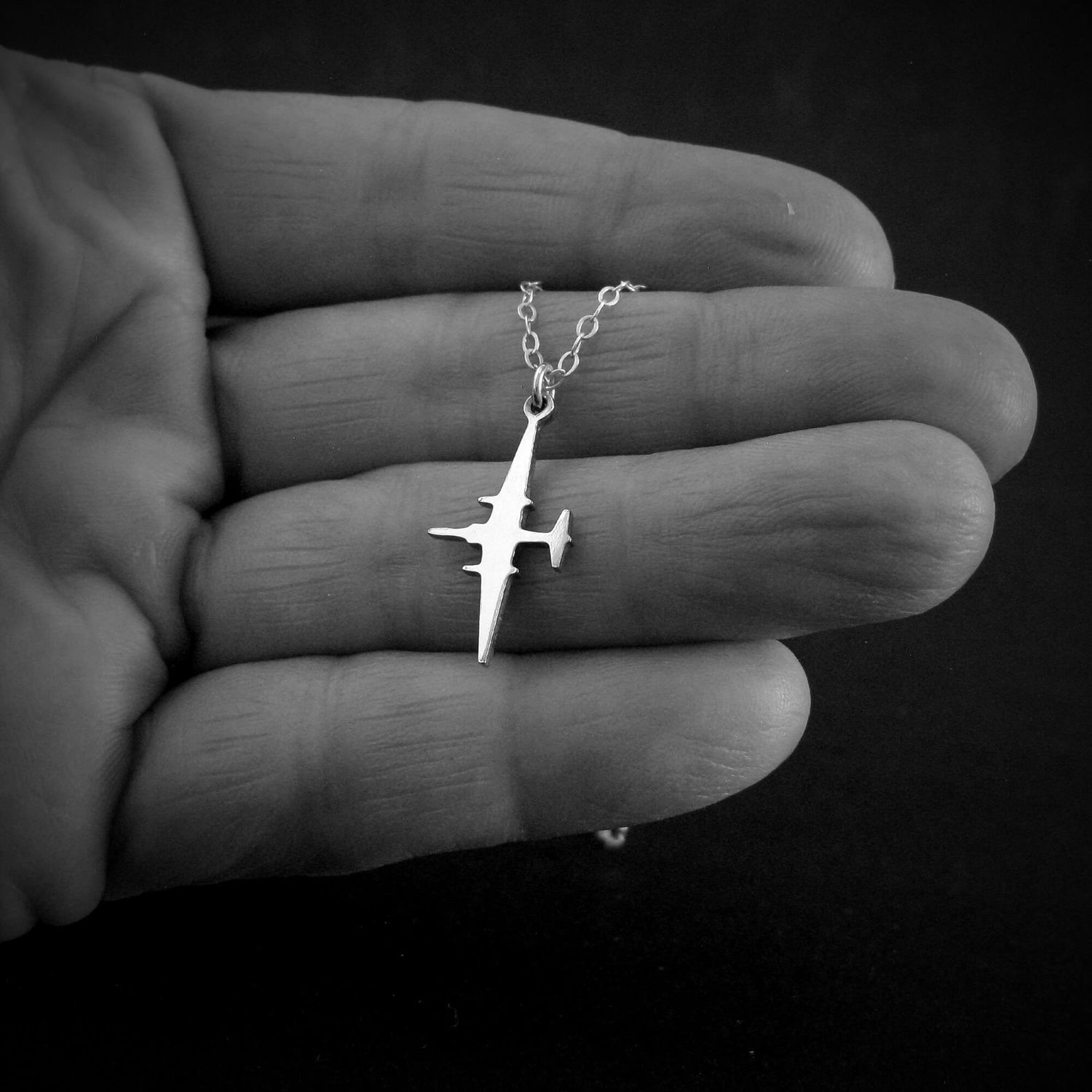 U-2 Dragon Lady military jet pendant necklace in sterling silver, displayed in the palm of a hand against a black background