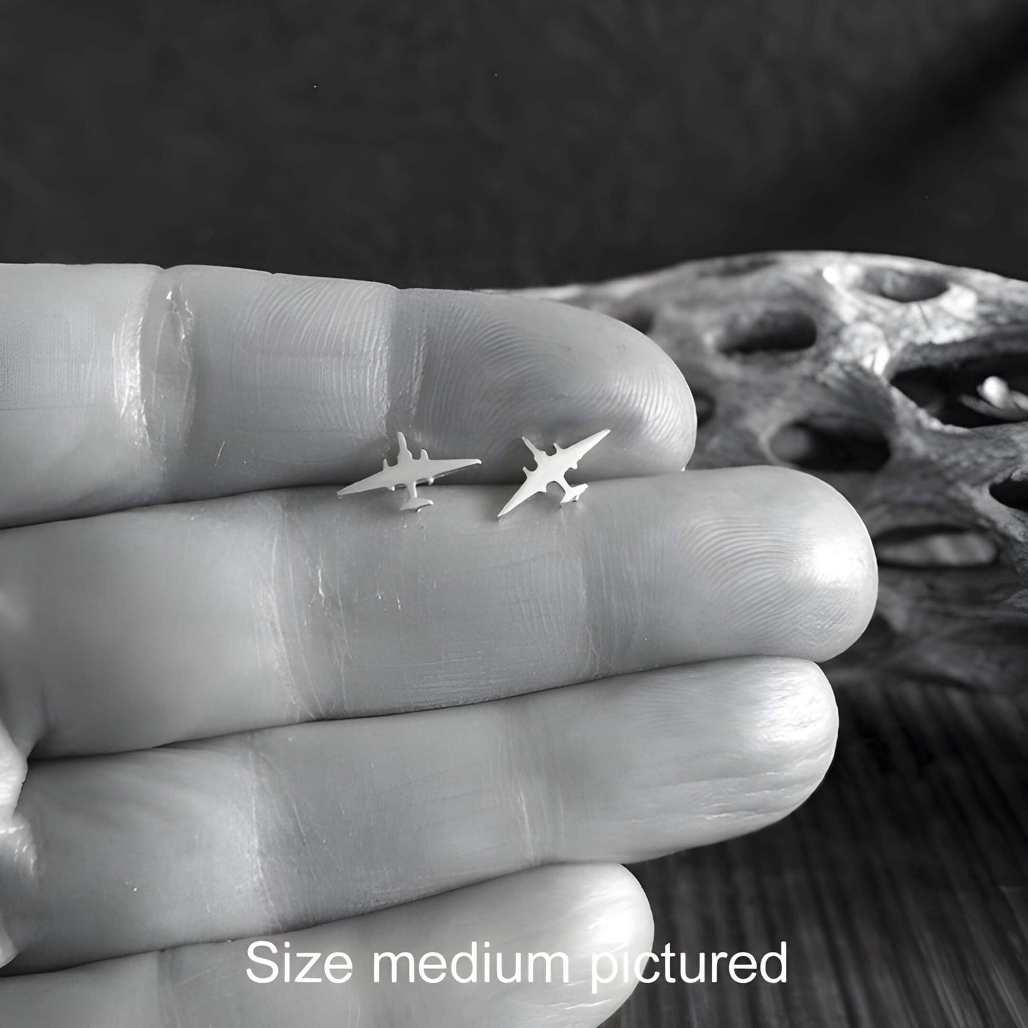 Pair of sterling silver U-2 Dragonlady Jet Fighter stud earrings held in a hand between fingers close up