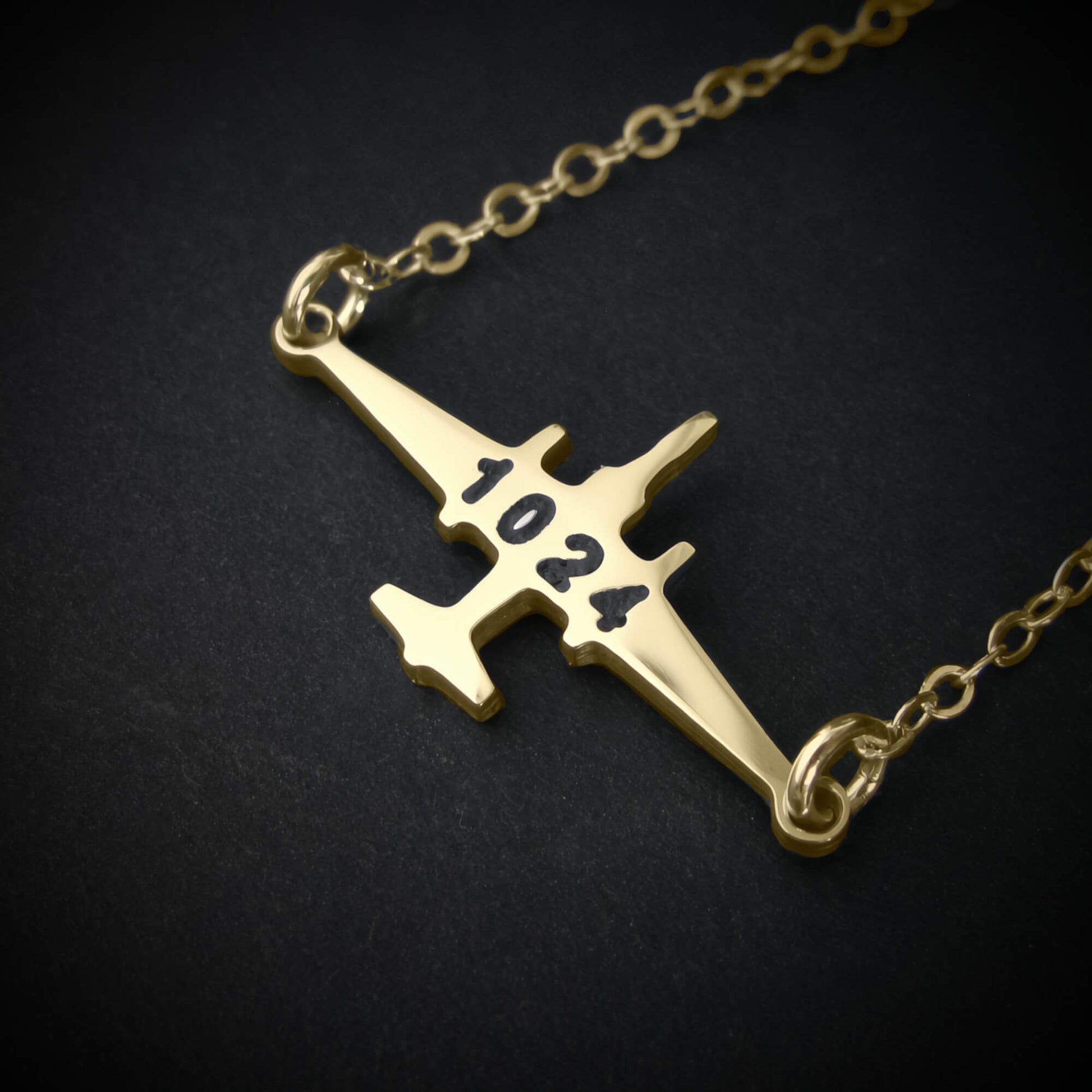 U-2 Dragon Lady military jet pendant necklace in 14k gold with engraved number “1024,” displayed close-up against a dark background.
