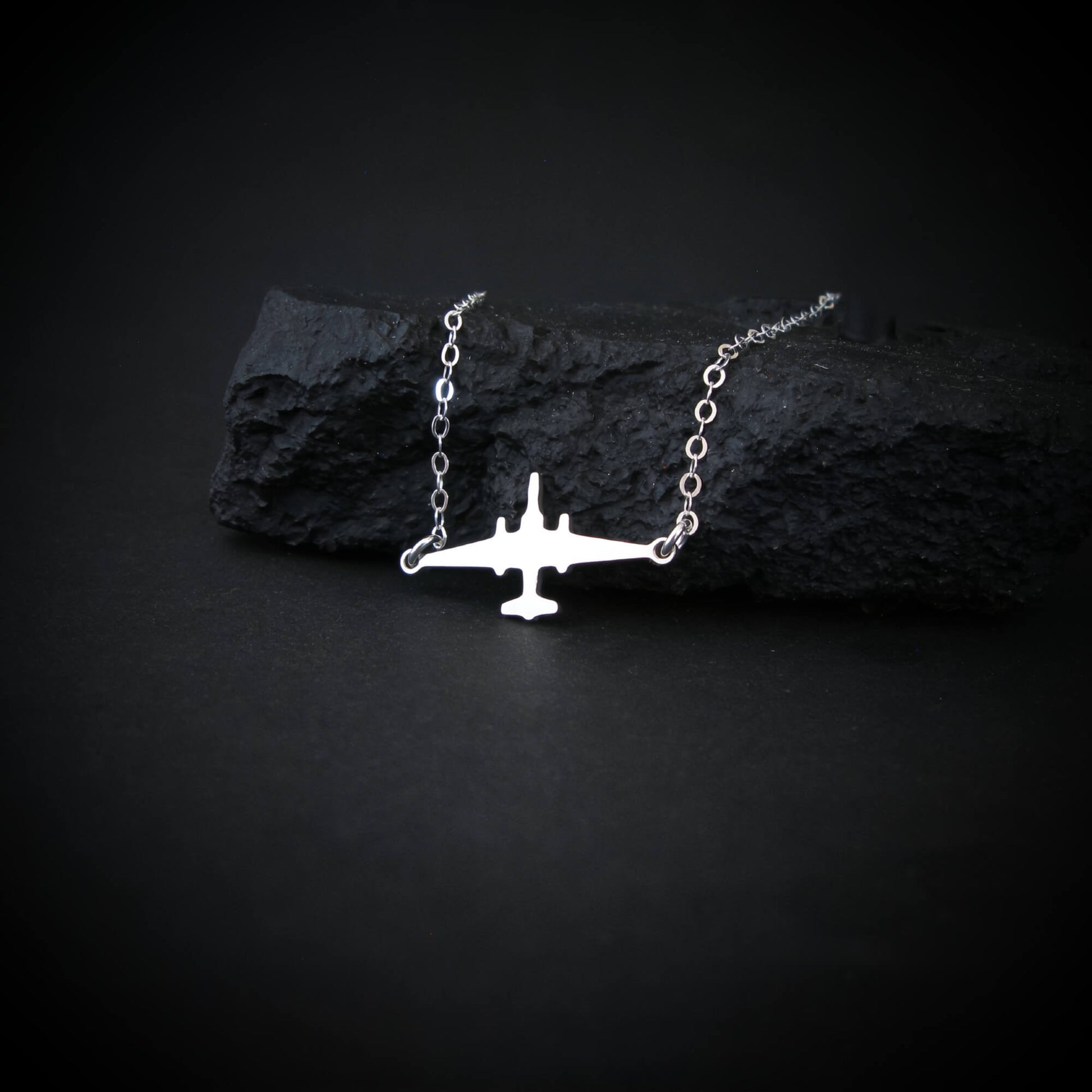 U-2 Dragon Lady military jet pendant necklace in sterling silver, displayed draped over a textured black rock on a dark background.