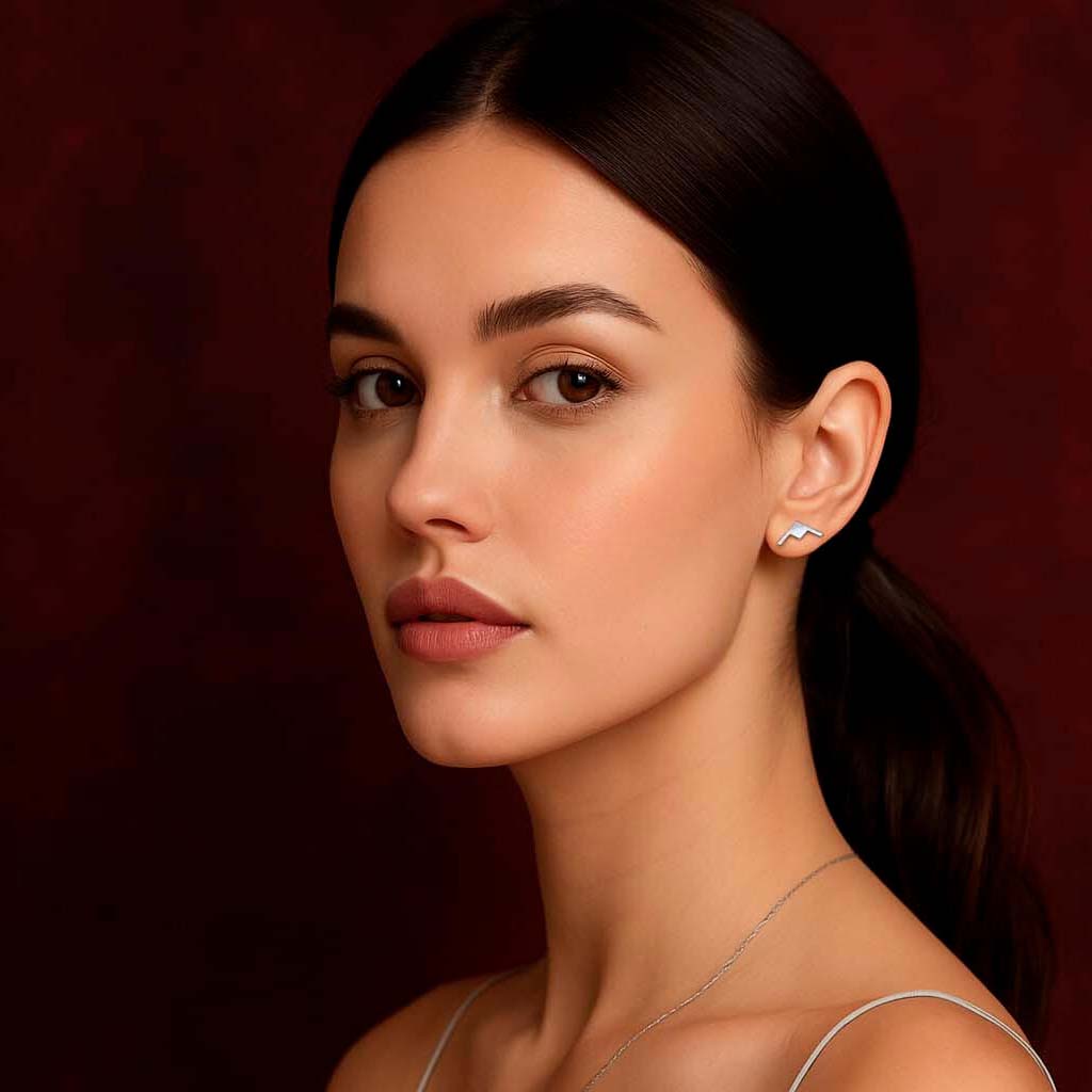 Woman wearing a delicate B-21  earring against a dark red background