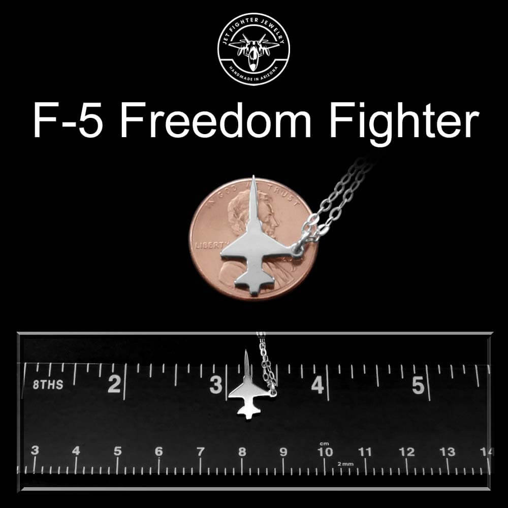 F-5 Freedom Fighter jet necklace pendant on a penny with a ruler for scale against a black background