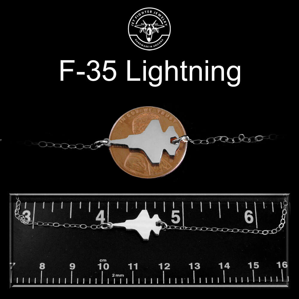 Necklace with F-35 Lightning design on a black background with a ruler for scale.