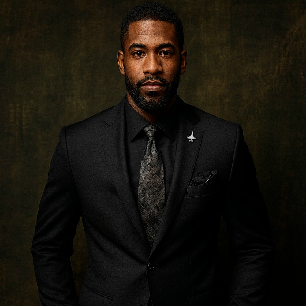 Man wearing a black suit with a silver F-16 lapel tie tack pin and patterned tie against a dark background