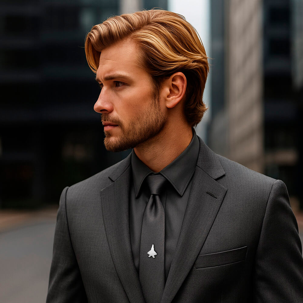 Man in a gray suit with a F-22 Raptor tie pin, standing outdoors.