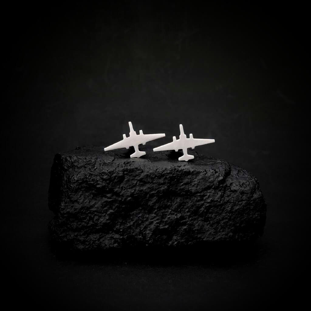 Two U-2 Dragon Lady airplane-shaped cuff links on a dark stone surface with a black background