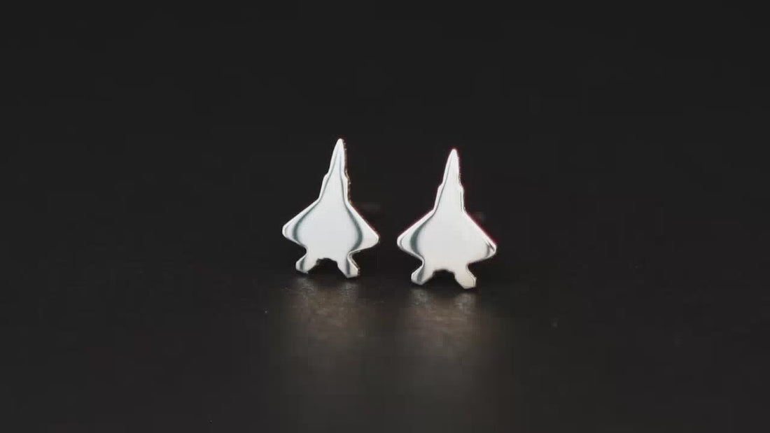 Pair of sterling silver F-22 fighter jet stud earrings shown on a turntable with a dark background